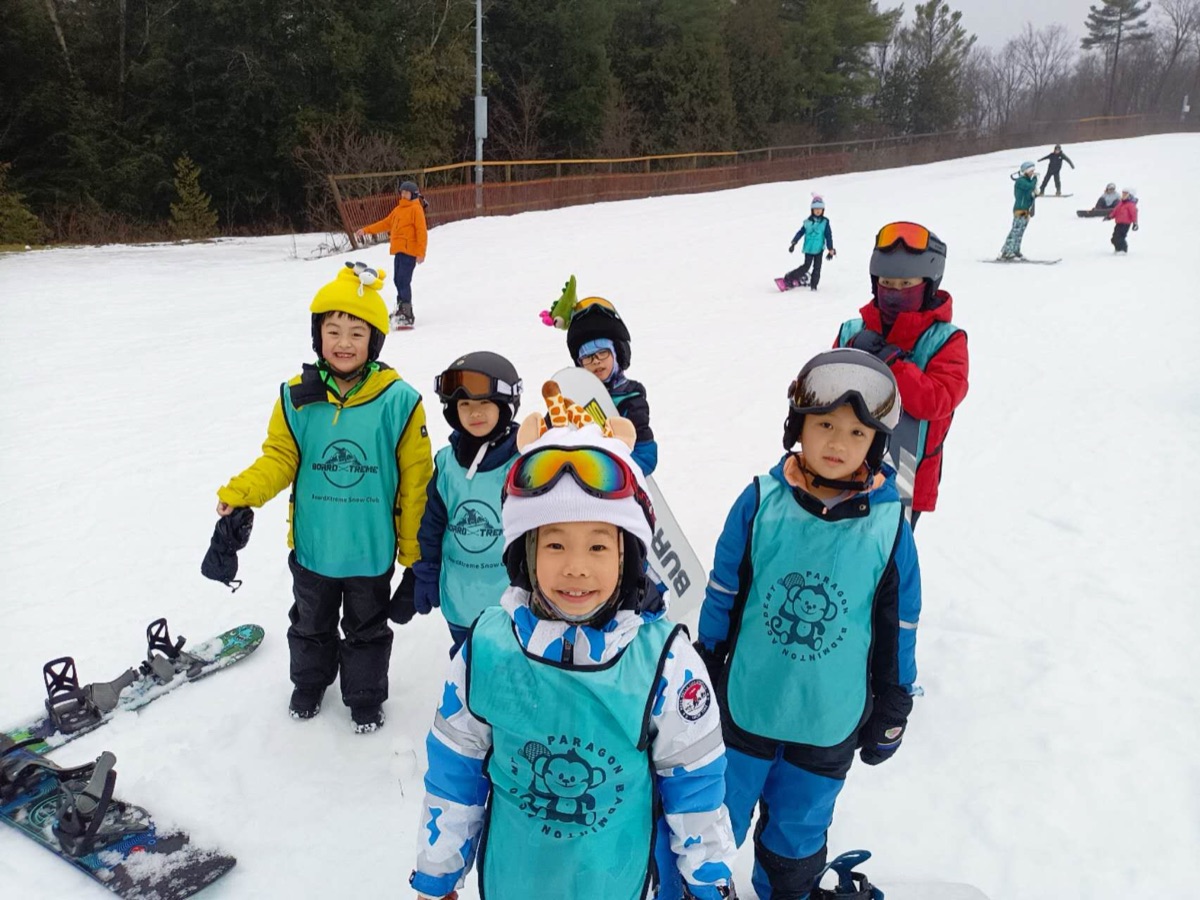 Smiling young students in BoardXtreme bibs on the slope
